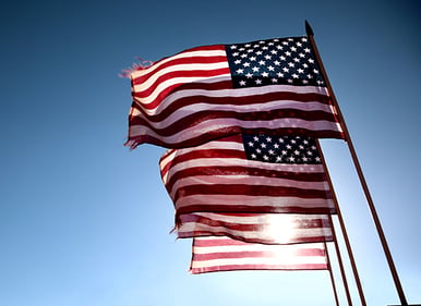 four-american-flags-fly-in-breeze-with-sun-behind-1
